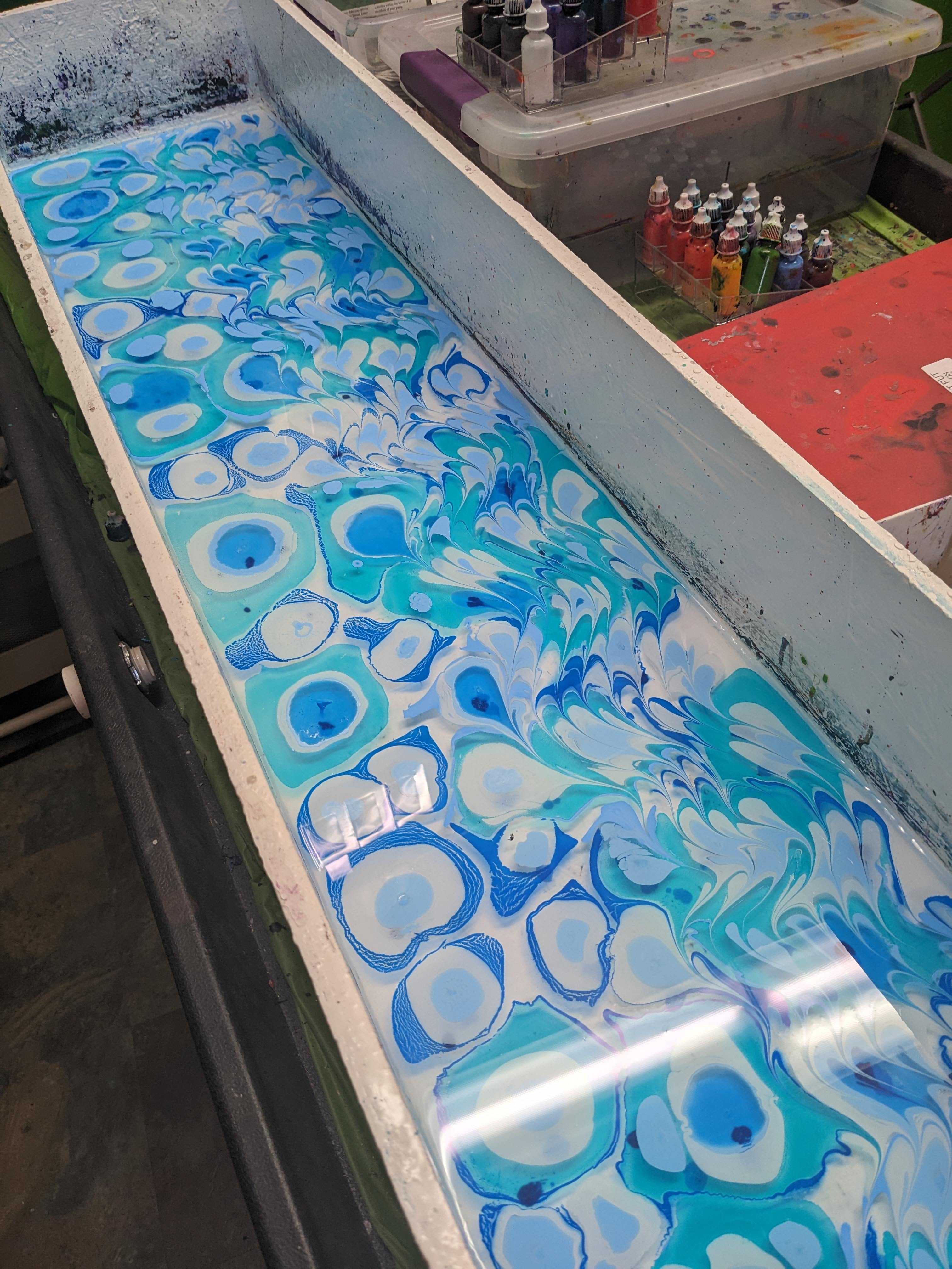 Water marbling tray with blue dots on the left, the dots have been swirled together on the right.