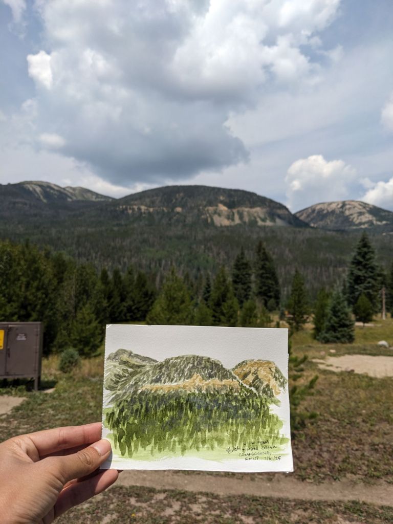 Watercolor of hills held in front of the hills; horizontal line of tan on the hills and watercolor represents the Grand Ditch