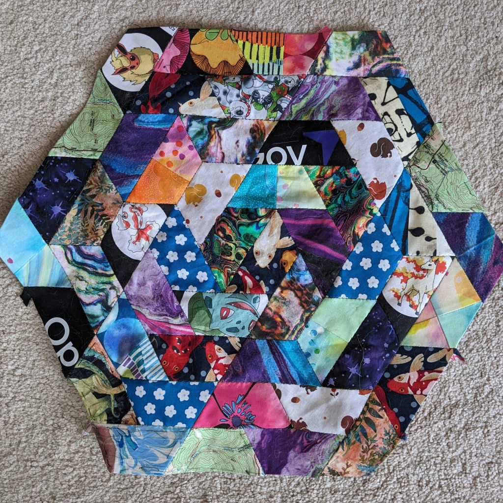 Hexagon made of trapezoids of many different fabrics, it is colorful and mismatched. Some fabrics are repeated but not next to each other.
