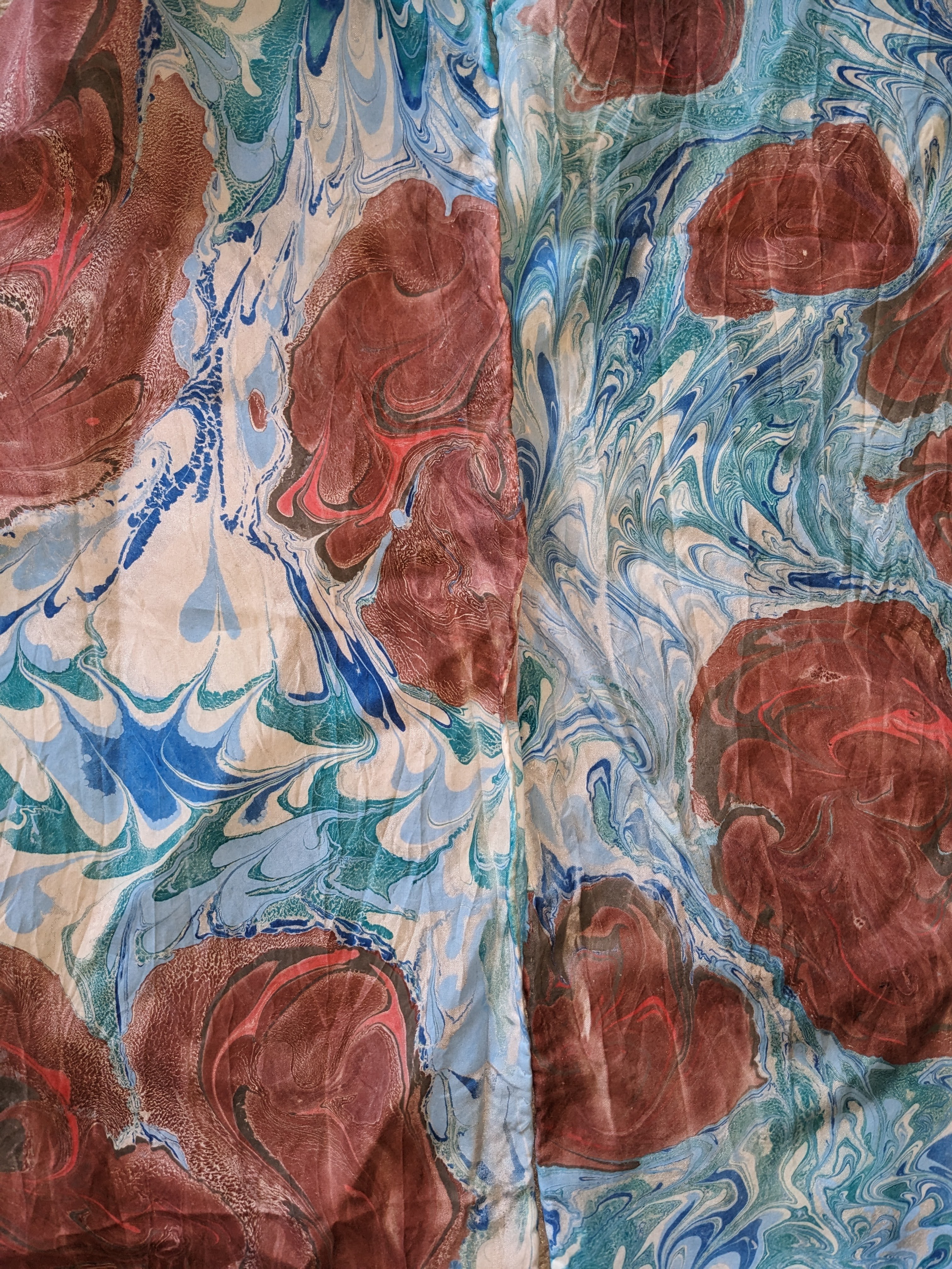 Closeup of fabric that has been marbled with blue swirled background and blobs of red, brown, and black.