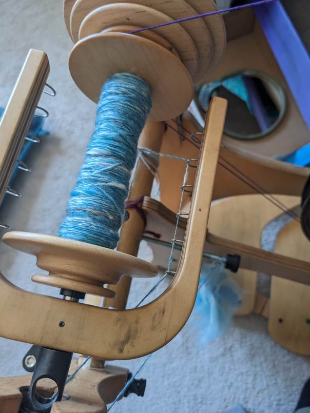 close up of blue fiber being spun onto a spinning wheel bobbin