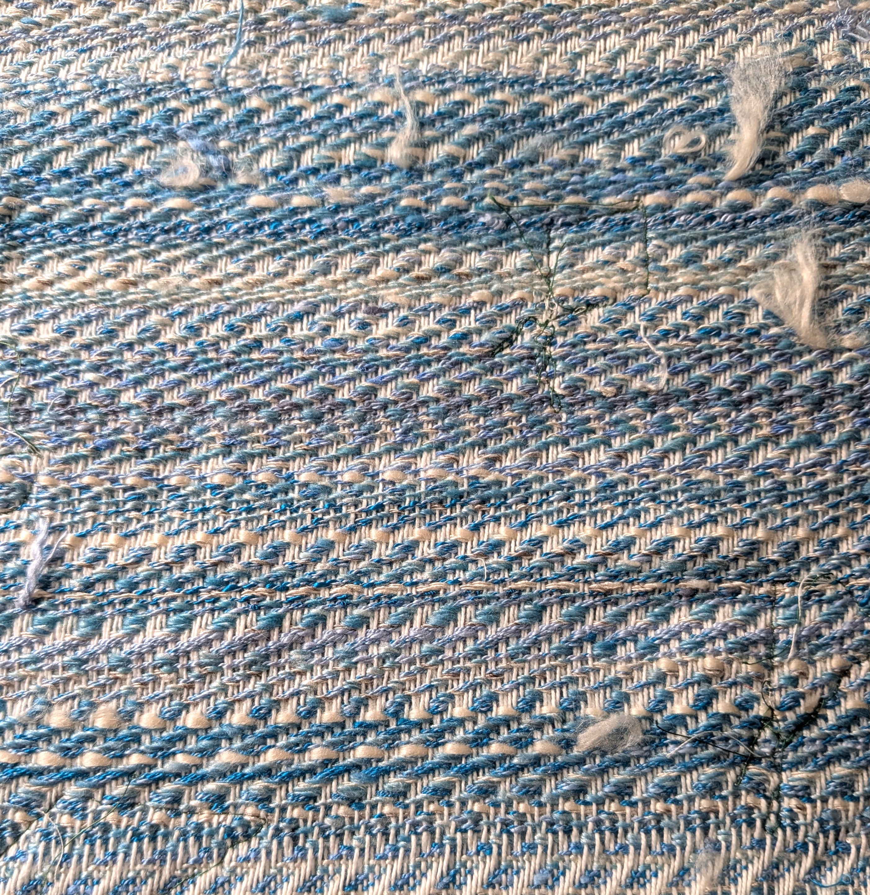 handwoven fabric with some stitches in green and fluffy bits of fiber sticking out